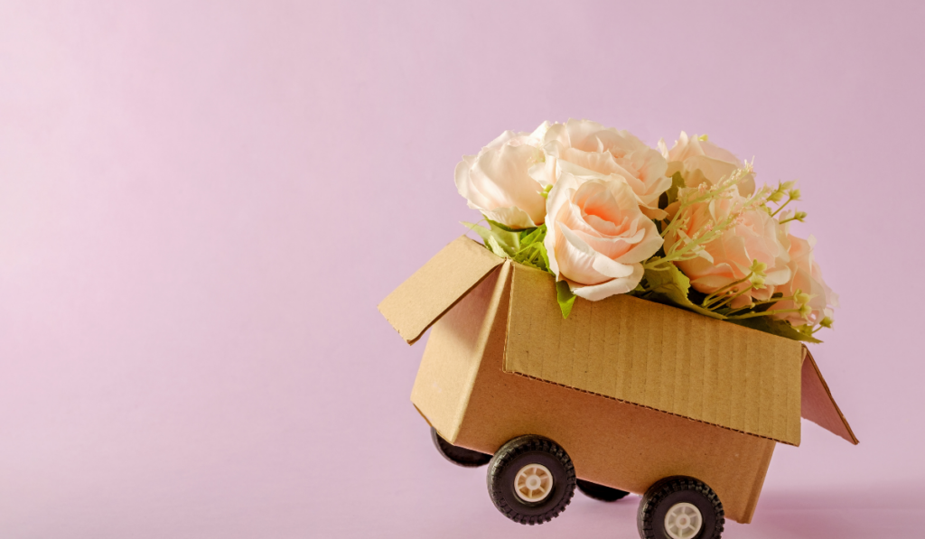 Cardboard box delivery container with truck wheels and bouquet of pink roses.