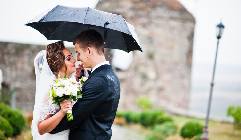 Wedding couple walking under rain with umbrella background tower of old castle