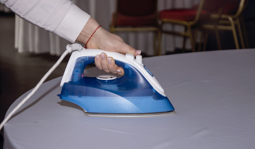 A female waiter in a restaurant irons a tablecloth with an iron before the celebration 