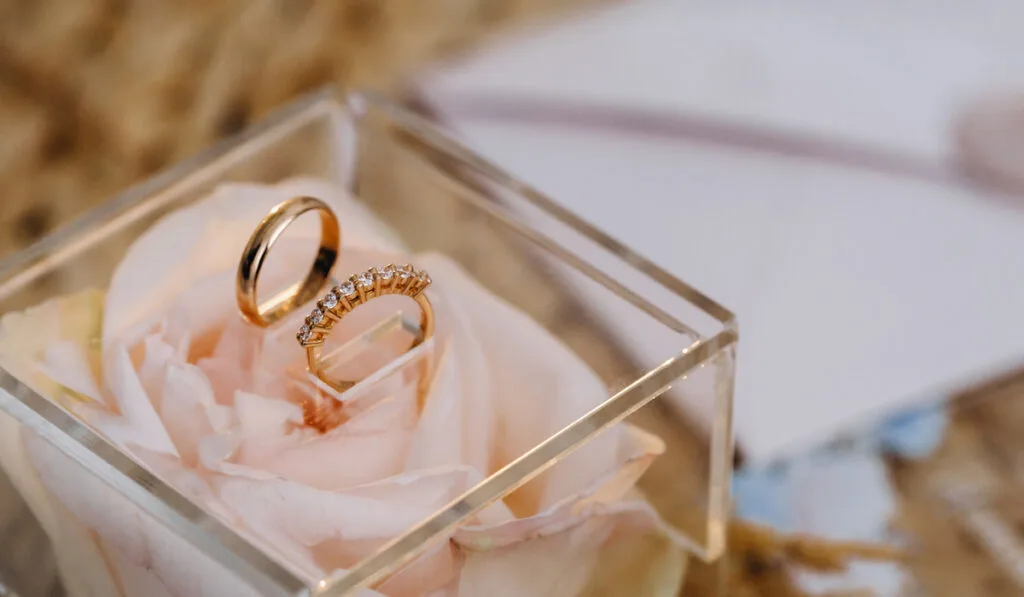 A pair of gold wedding rings inside glass box with flower