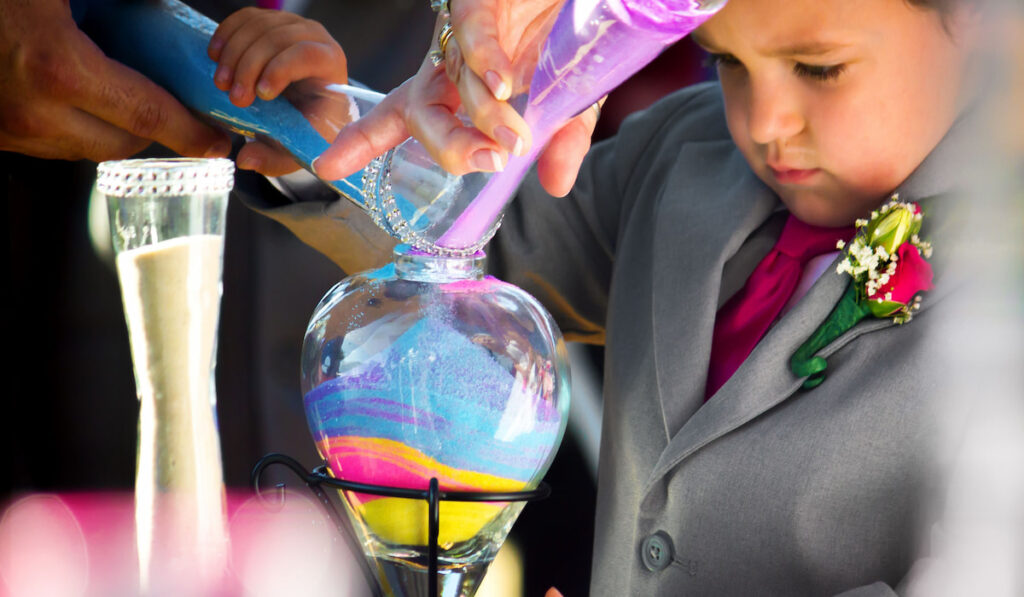 A ring bearer, who is the son of the bride, pours colored sand in the unity ceremony during a wedding 