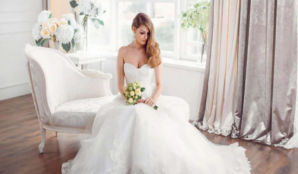 Beautiful bride wearing white wedding dress sitting on a couch 