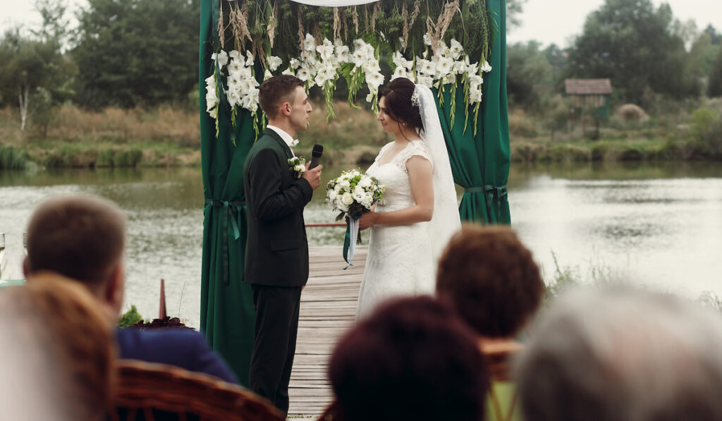 Beautiful couple, groom giving wedding vow at wedding ceremony near lake