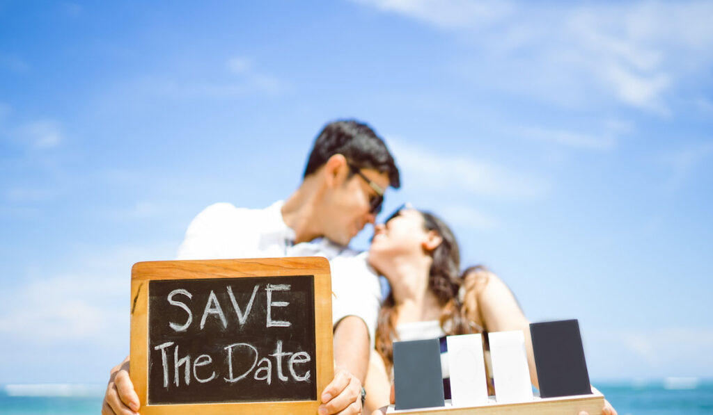 Bride and Groom kissing and showing chalkboard text save the date on the beach 
