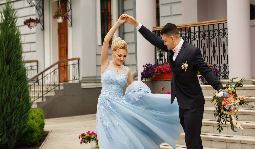 Bride wearing blue wedding dreaa and groom holding bouquet dancing 