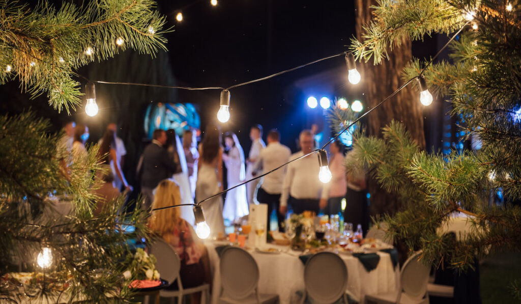 Decorative outdoor lighting lamps in the forest at a wedding party with blurry image of newlyweds with their guest 