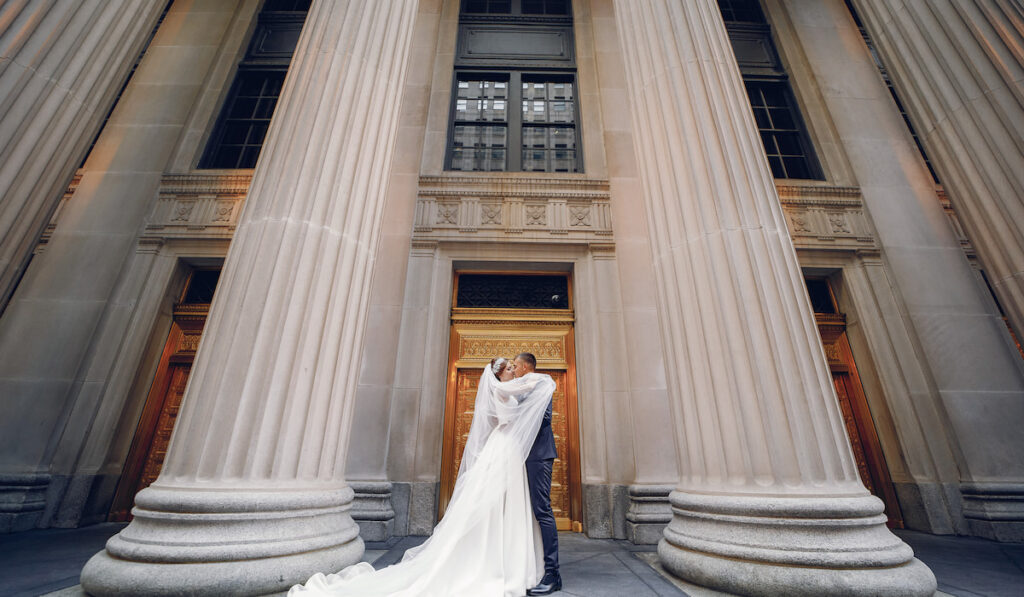 Elegant bride in a white dress and veil. Handsome groom in a blue suit. Couple near large building with columns

