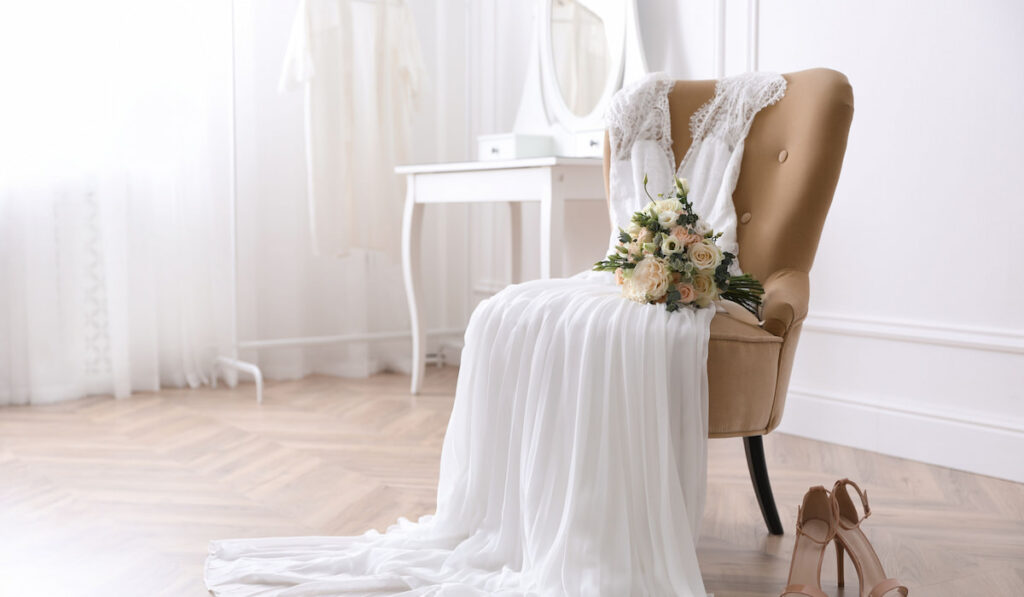 Elegant wedding dress, shoes and bouquet in room 
