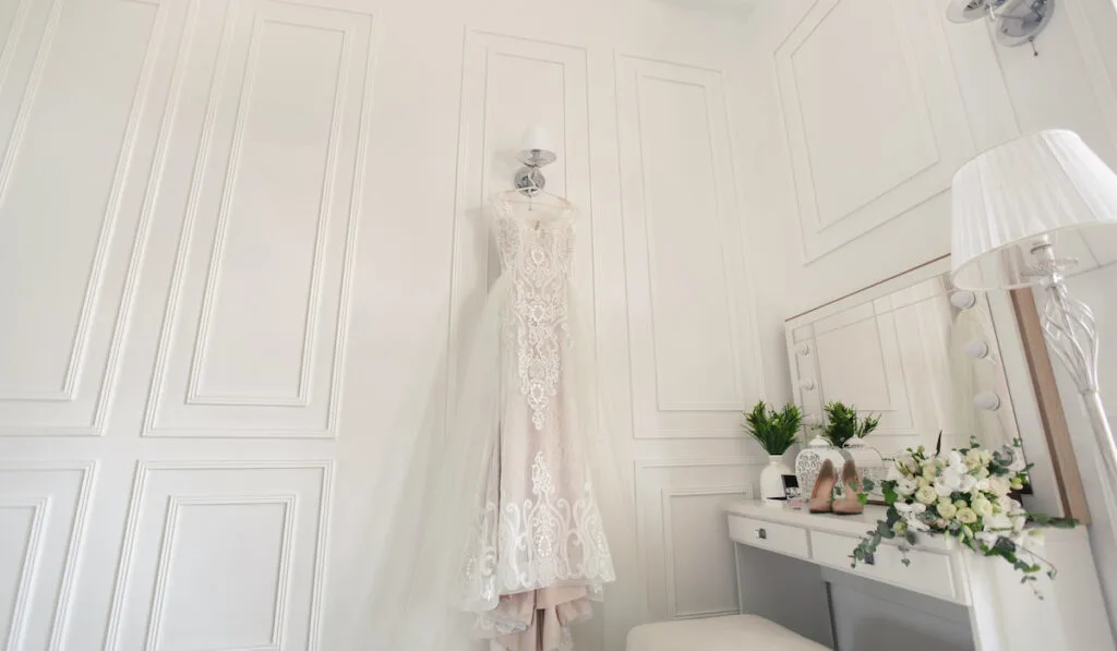 Elegant wedding white dress hanging on a wall during a wedding preparation.