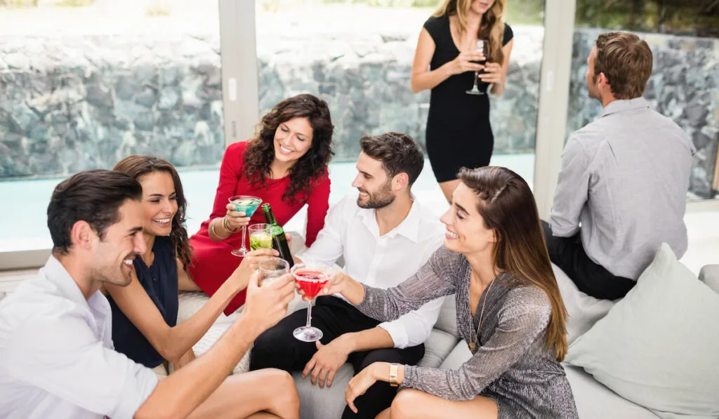 Group of friends toasting cocktail drinks and enjoying wedding party at home 