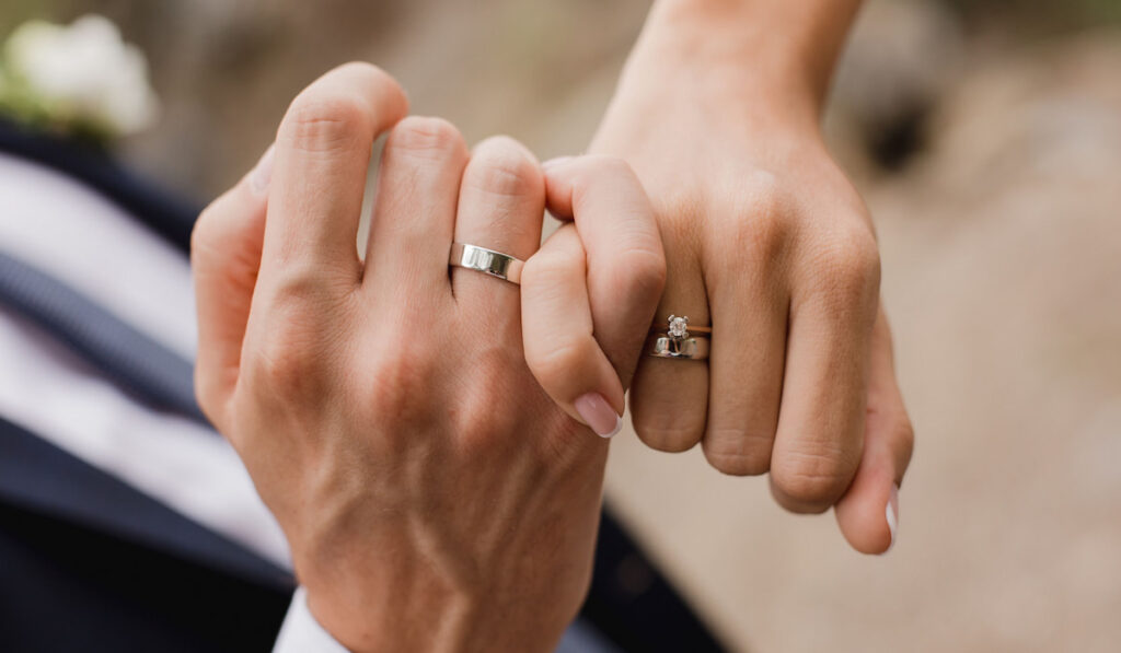 Hand of bride and groom showing their wedding ring and engagement ring