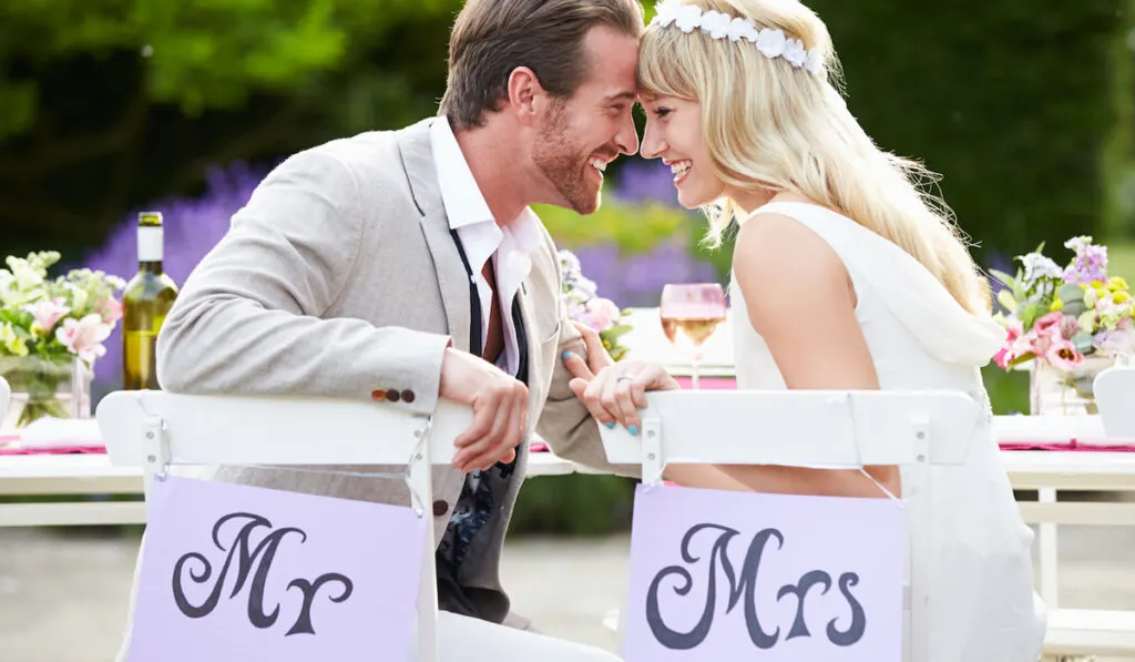 Mr and Mrs Wedding Sign. Happy bride and groom sitting on their chair with sign at wedding reception