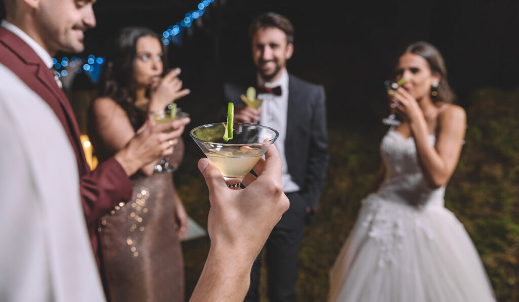 Happy friends drinking cocktails on a night field wedding party
