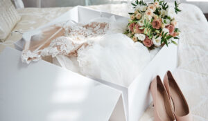 Luxury-wedding-dress-in-white-box-beige-womens-shoes-and-bridal-bouquet-on-bed