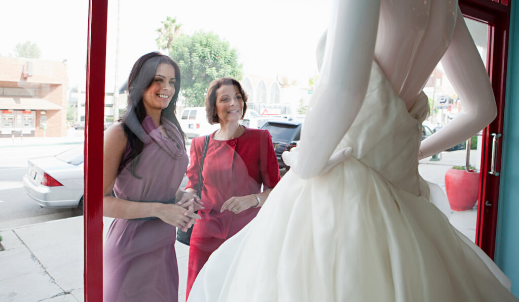 Mother and daughter looking at wedding dress in shop window
