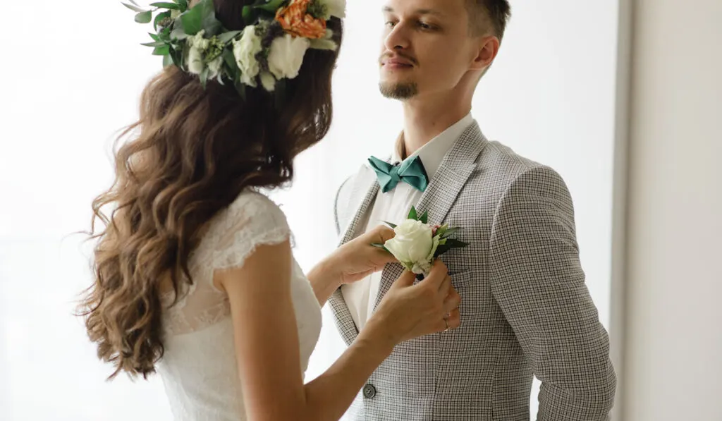 The bride puts a boutonniere on the groom's suit
