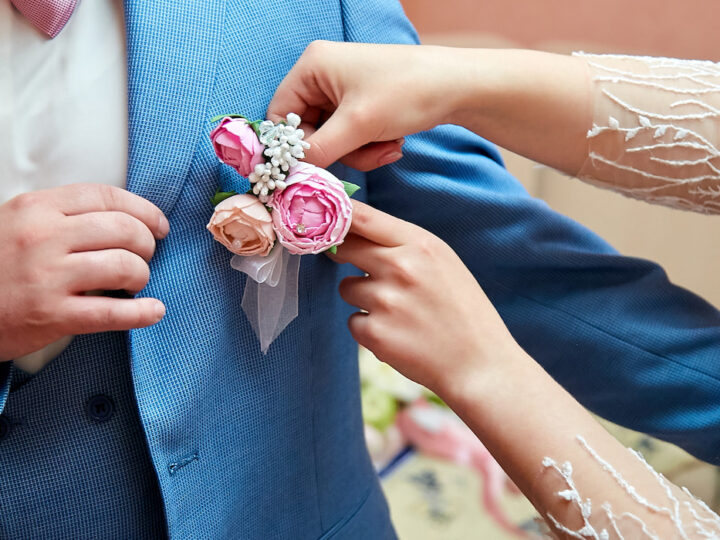 The-brides-hand-puts-on-a-boutonniere-flower-on-the-grooms-jacket