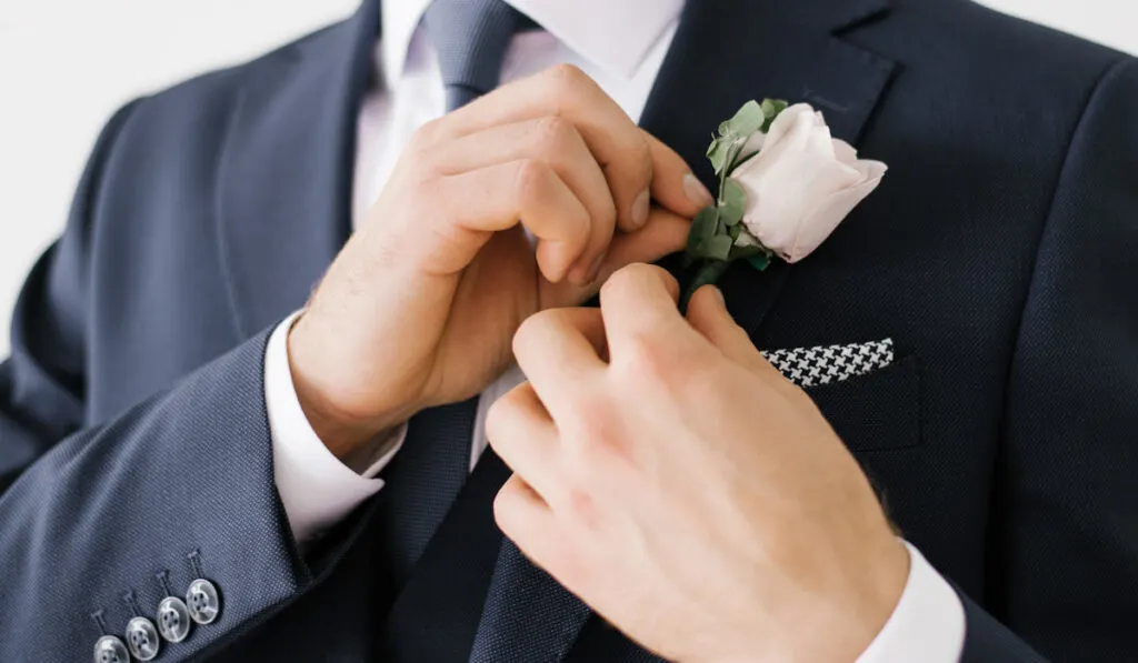 The groom fastens a pink rose boutonniere to his jacket
