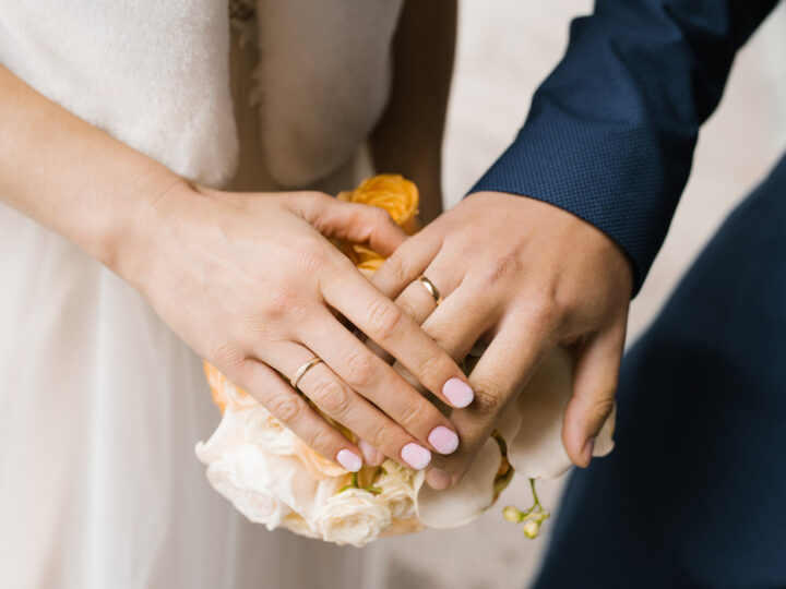 The hands of the bride and groom with wedding rings on the wedding bouquet