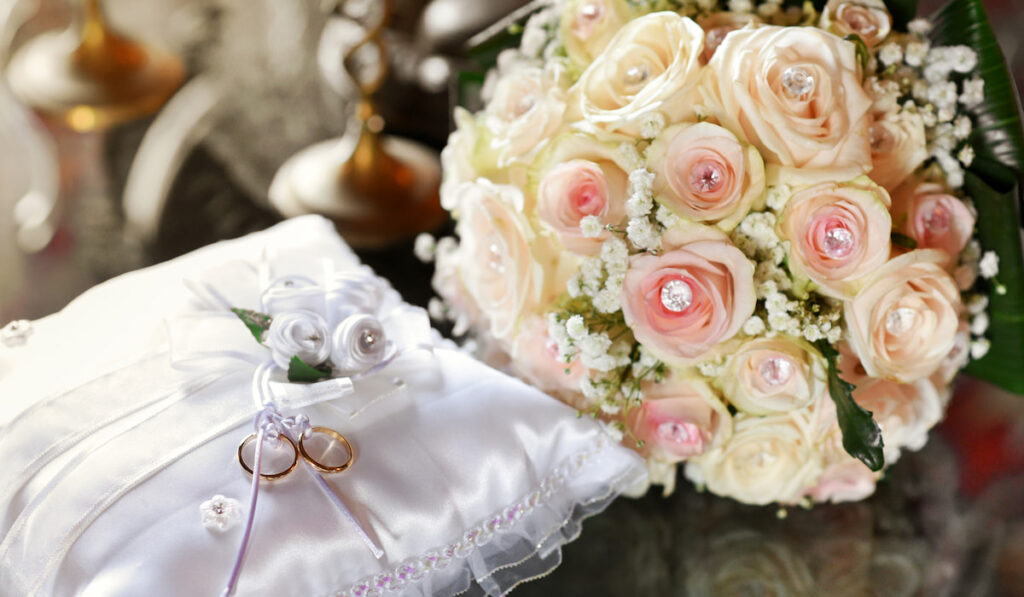 Two gold wedding rings displayed on cushion with bridal bouquet
