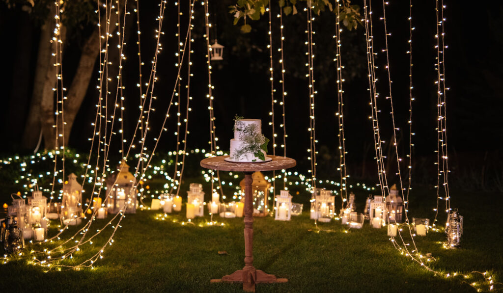 Wedding cake on a table surrounded by lights on backyard