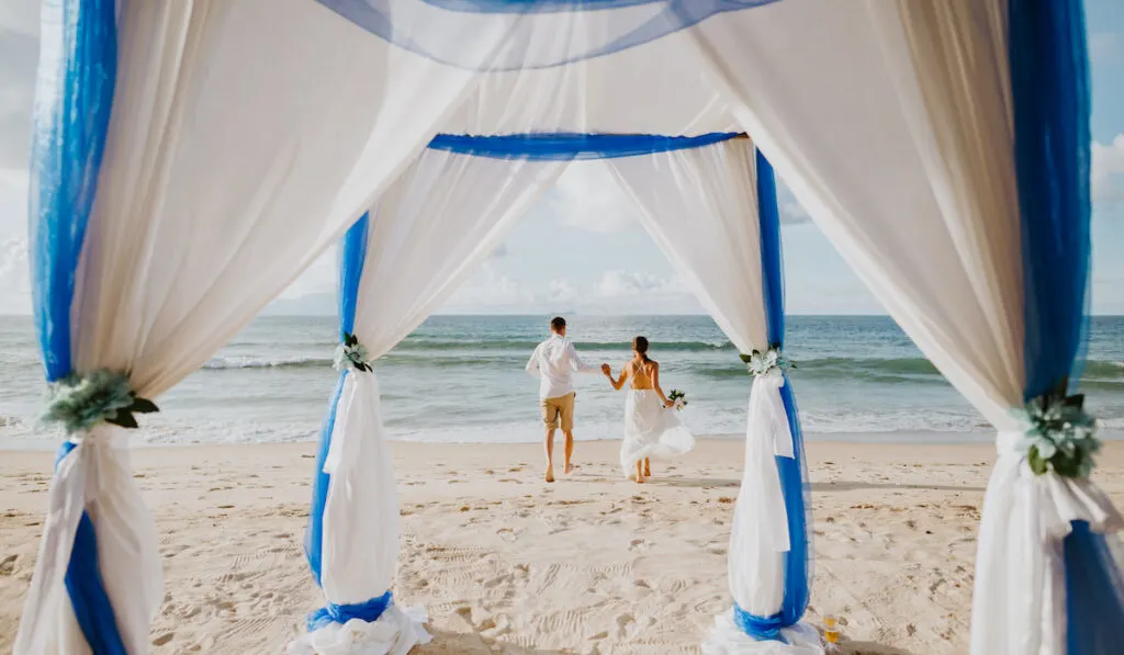 Wedding couple on beach with wedding arch background. Destination wedding on the island with sea view.