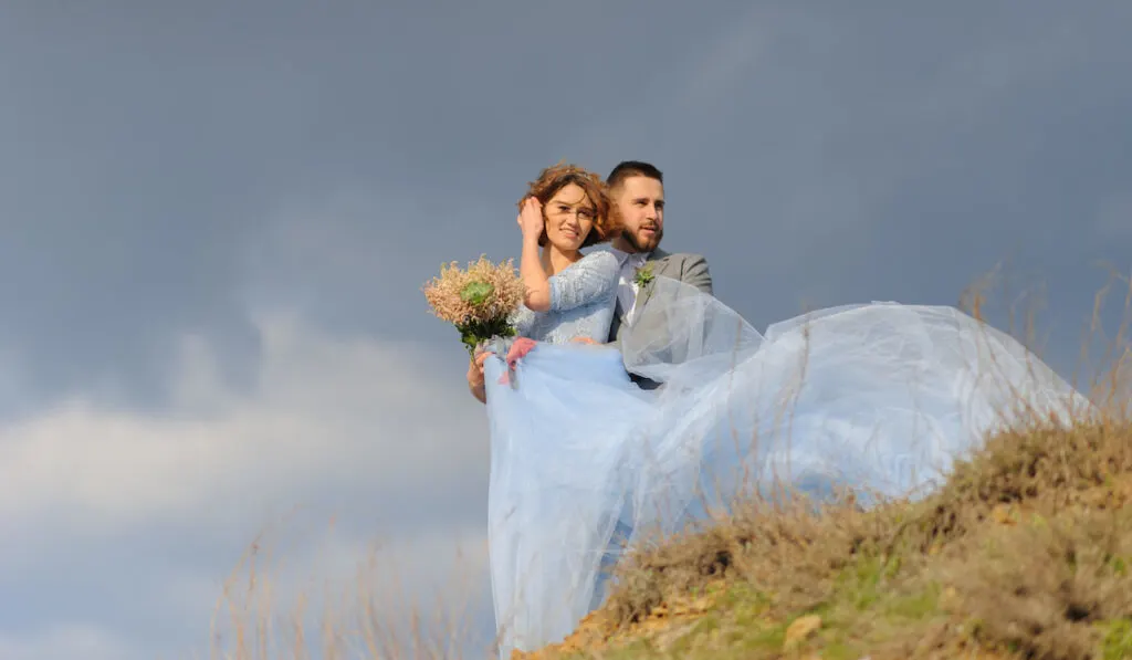 Wedding photo session of newly wed couple, bride wearing blue dress and holding bouquet