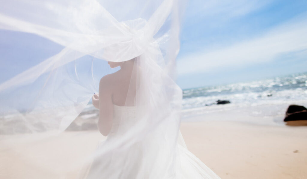 back view of the bride on her wedding dress with veil on the beach