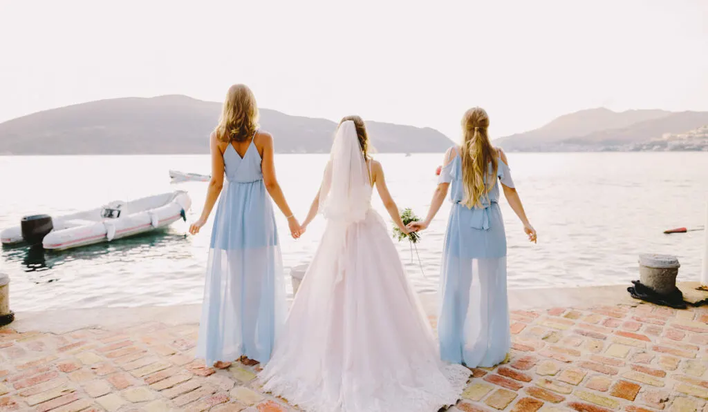 bridesmaids and bride facing the beach while holding their hands together