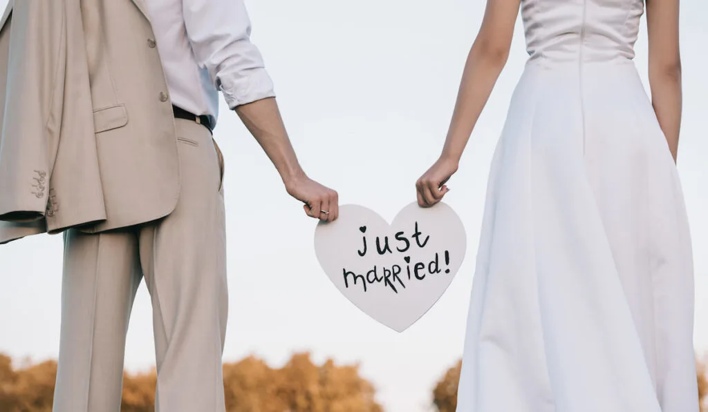 cropped shot of young wedding couple holding heart with just married inscription
