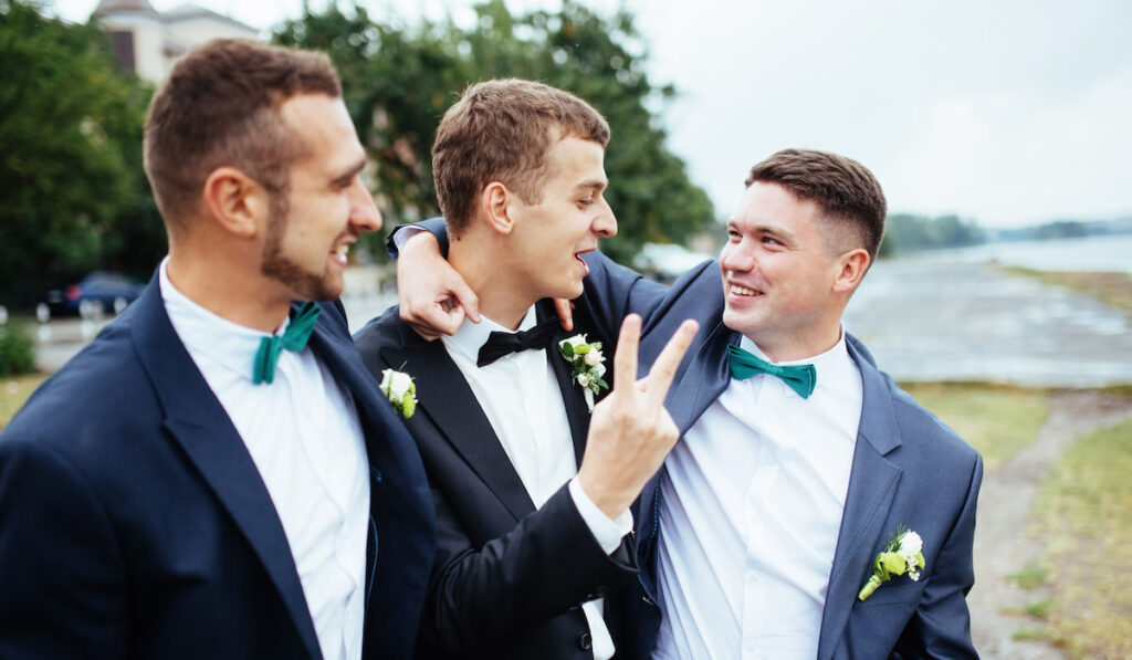 groom in black suit with two groomsman