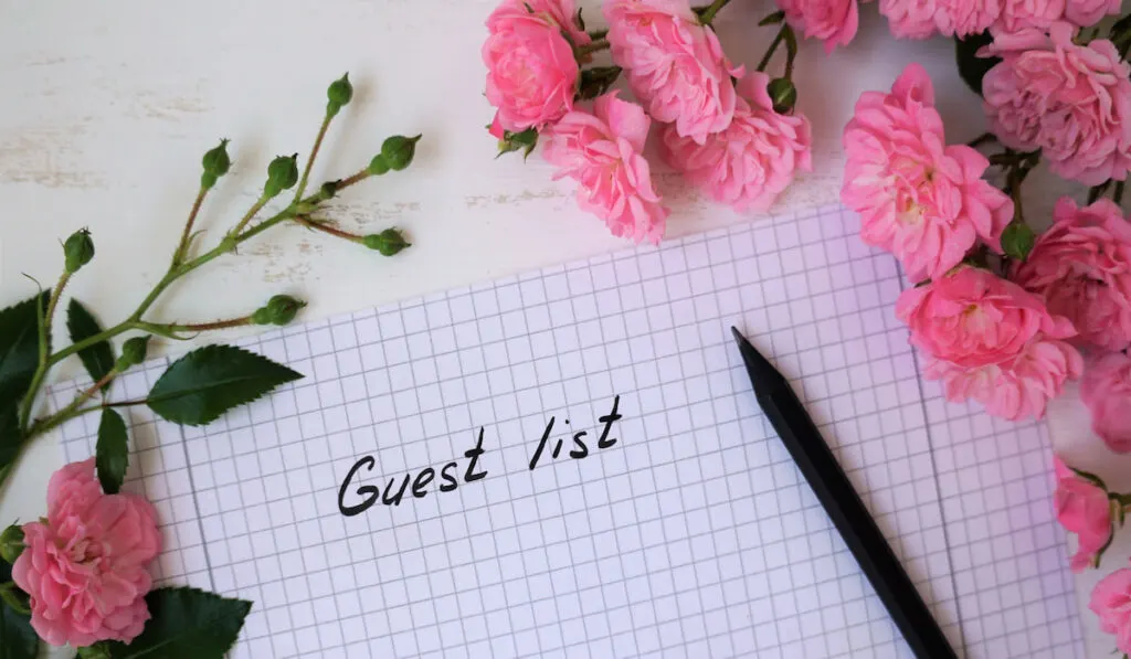 guest list on a paper with pen and flowers on background 
