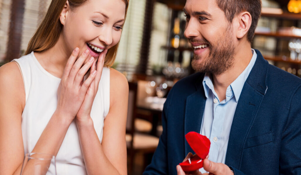 man making a proposal while giving an engagement ring to his girlfriend in restaurant