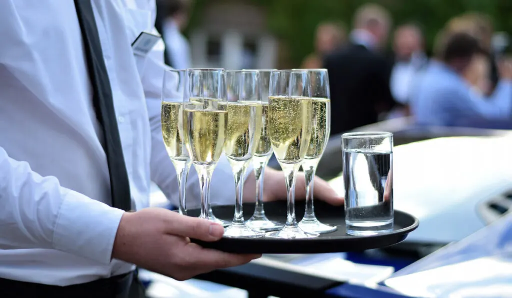 waiter holding a tray with champagne flutes and glass of water at wedding event