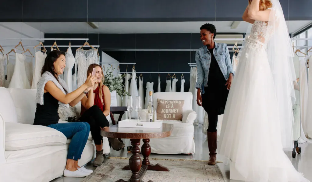 woman fitting wedding dress in a bridal shop with her friends 