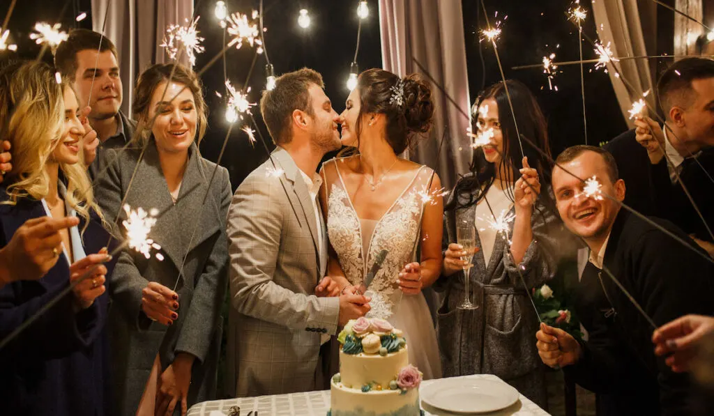 young beautiful wedding couple cut wedding cake with friends and have fun with bengal lights 