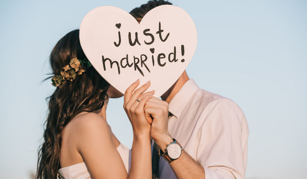 young wedding couple kissing and holding heart with just married inscription
