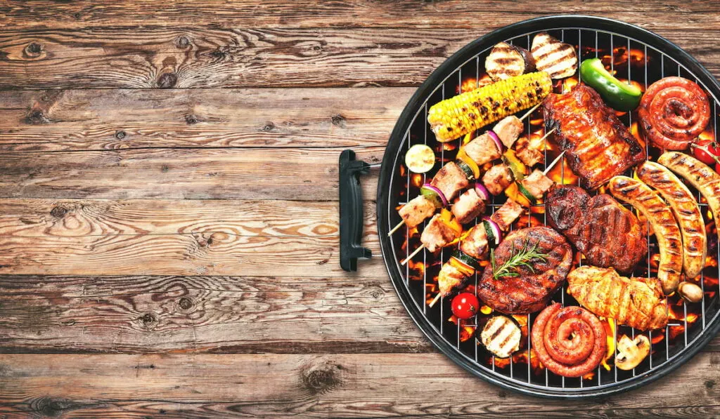 Assorted delicious grilled meat and bratwurst with vegetables over the coals on a barbecue on rustic wooden background