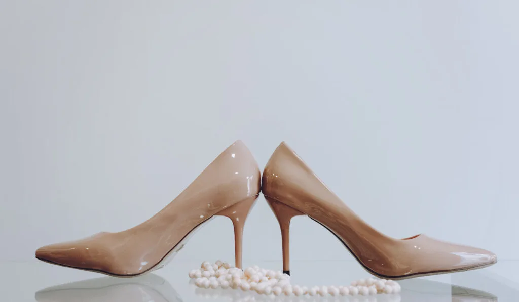 Beige high heels shoes and beads on glass table 