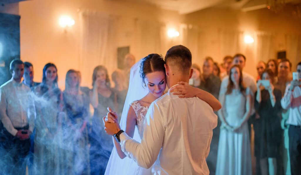 Blue and yellow lights shine around wedding guests and wedding couple dancing in the first time 