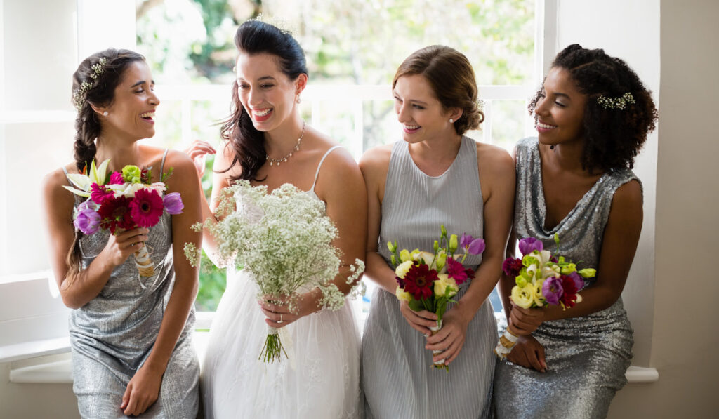 Bride and bridesmaids standing with bouquet in the hotel while preparing for wedding ceremony
