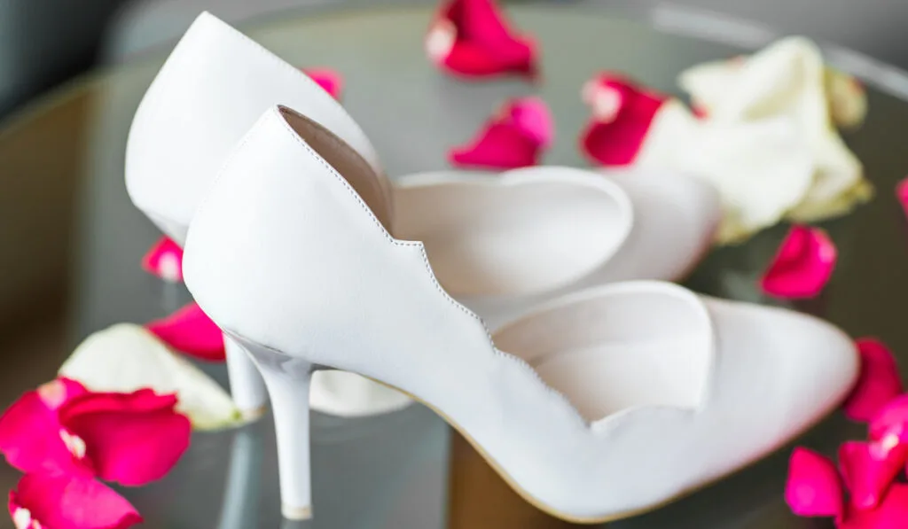 Elegant white shoes on a table with petals of rose 