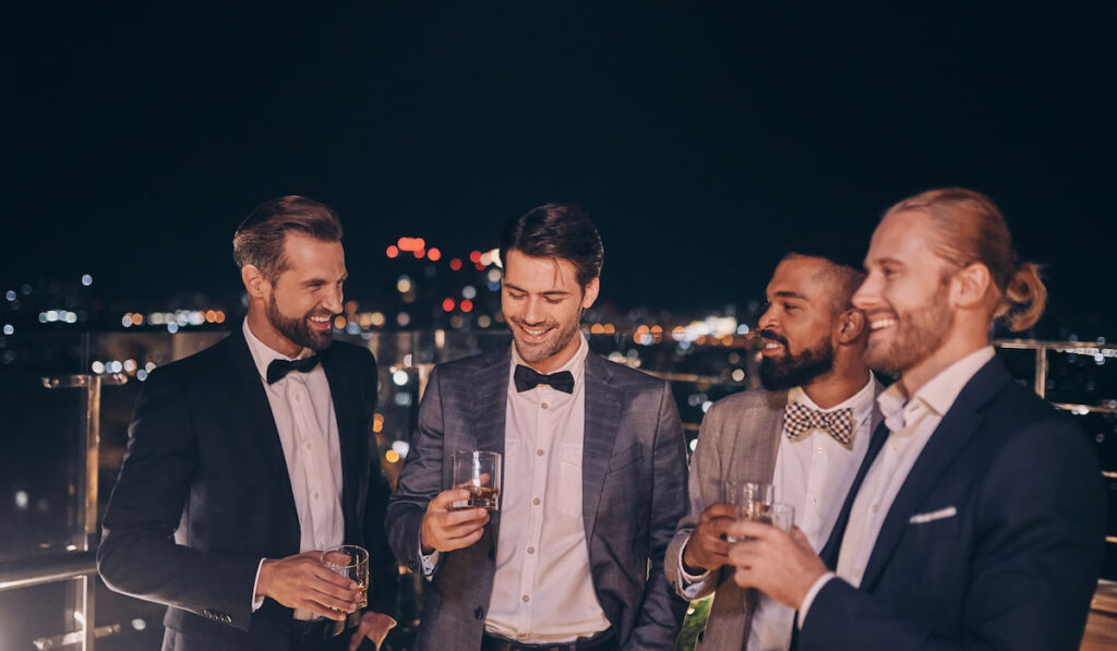 Groomsmen in different suits on wedding party drinking whiskey 