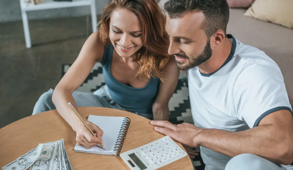 Happy couple planning about wedding budget with money, notebook and calculator on the table 