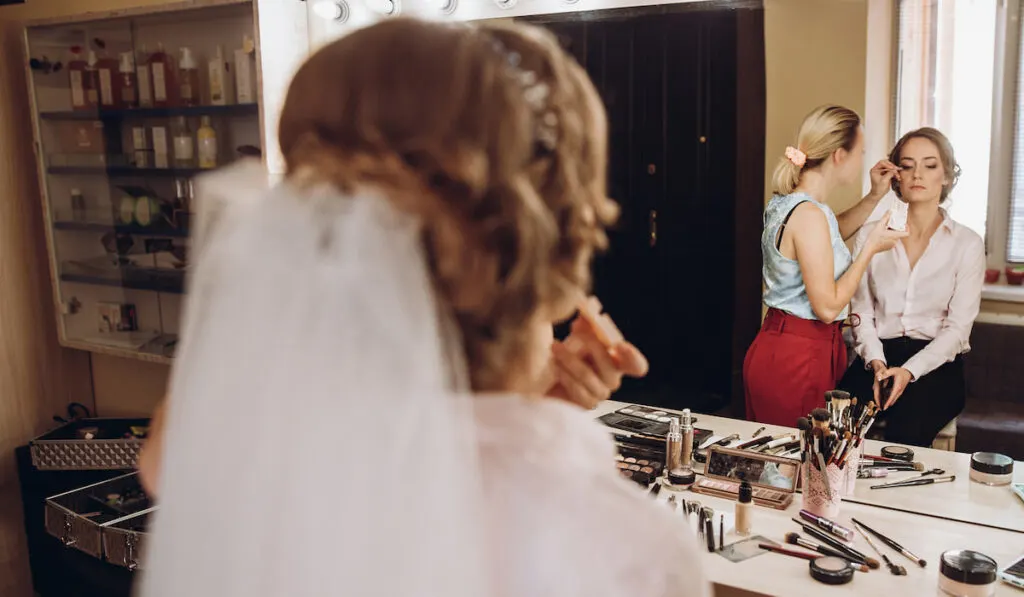 Professional stylist applying makeup on young beautiful bride
