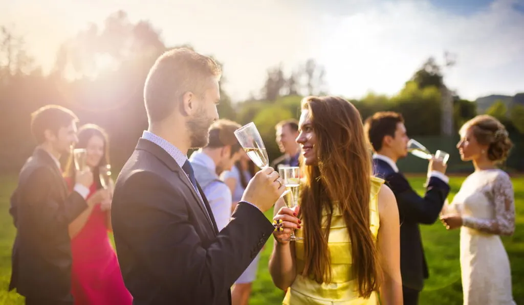 Wedding guests drinking champagne while the newlyweds clinking glasses in the background