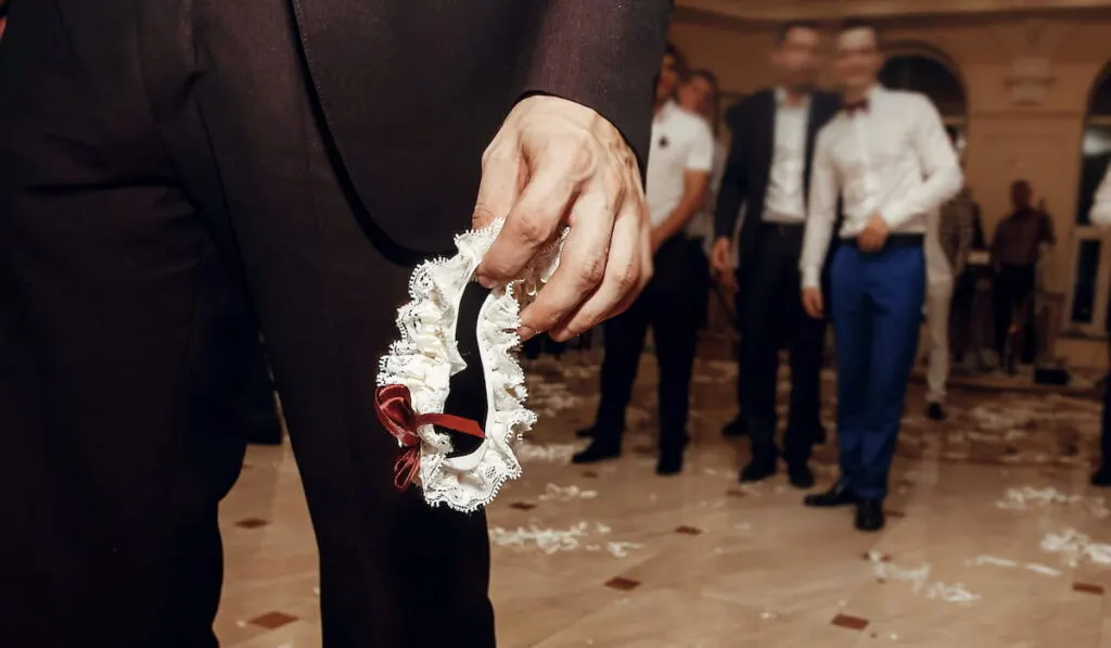 groom holding silk garter from bride at wedding party. tradition of throwing bridal garter to man