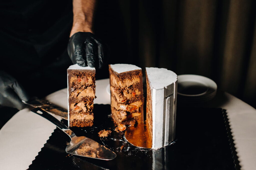A black-gloved chef is slicing a chocolate wedding cake