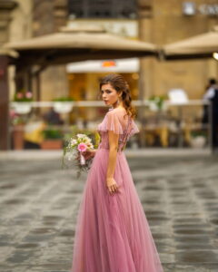 A bride in a pink dress with a bouquet stands in the center of the Old City of Florence in Italy - ee220805