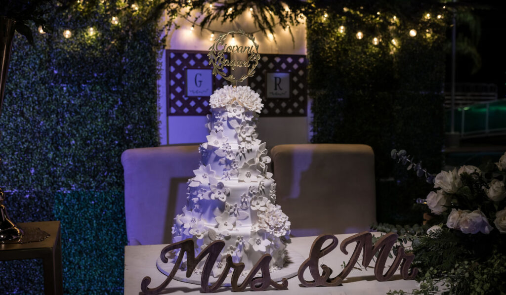 A four tiered wedding cake adorned with many sugar flowers, displayed at the reception

